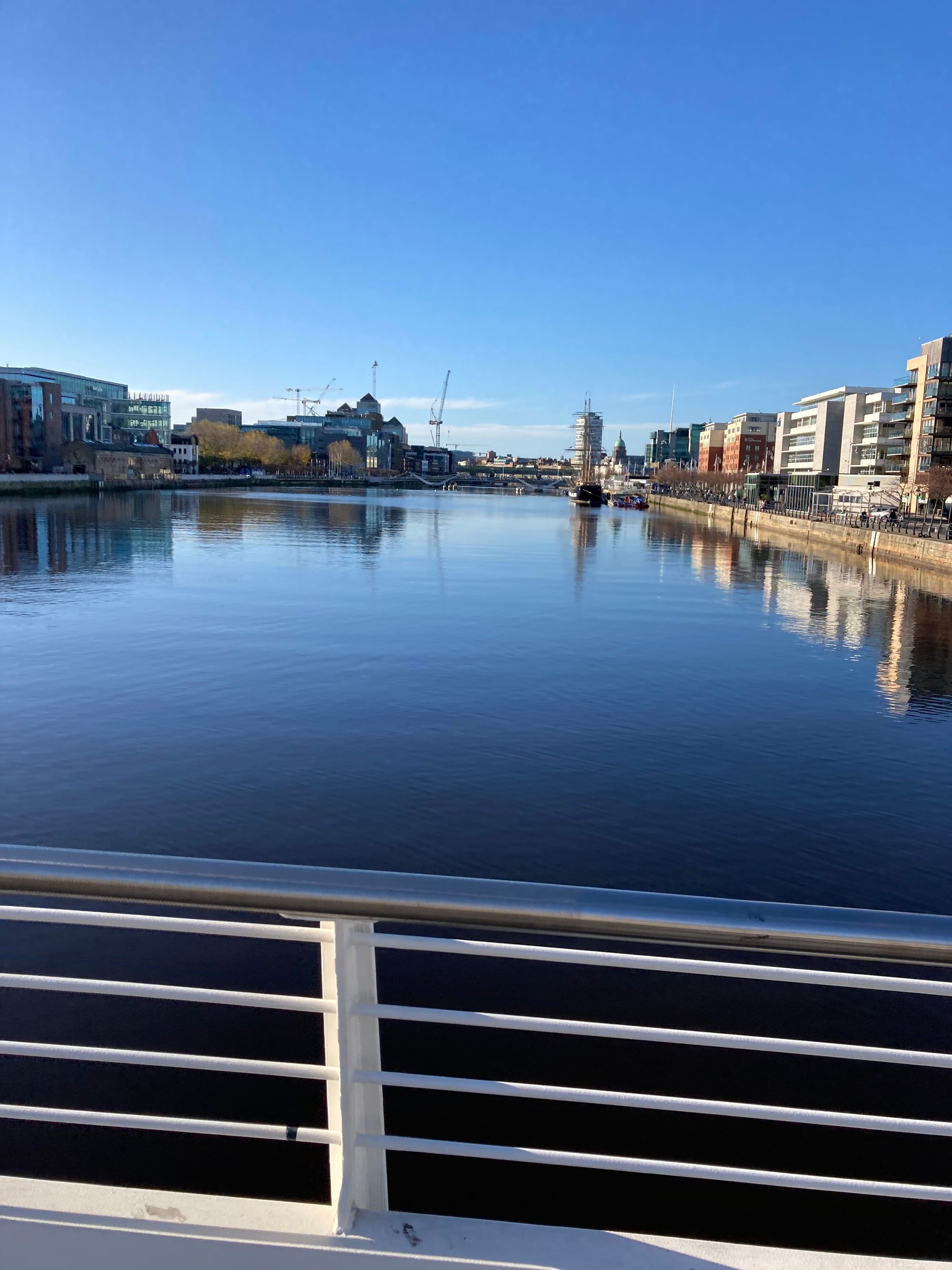 An image of the River Liffey on sunny day. You can see buildings on the side and a railing before the river starts.