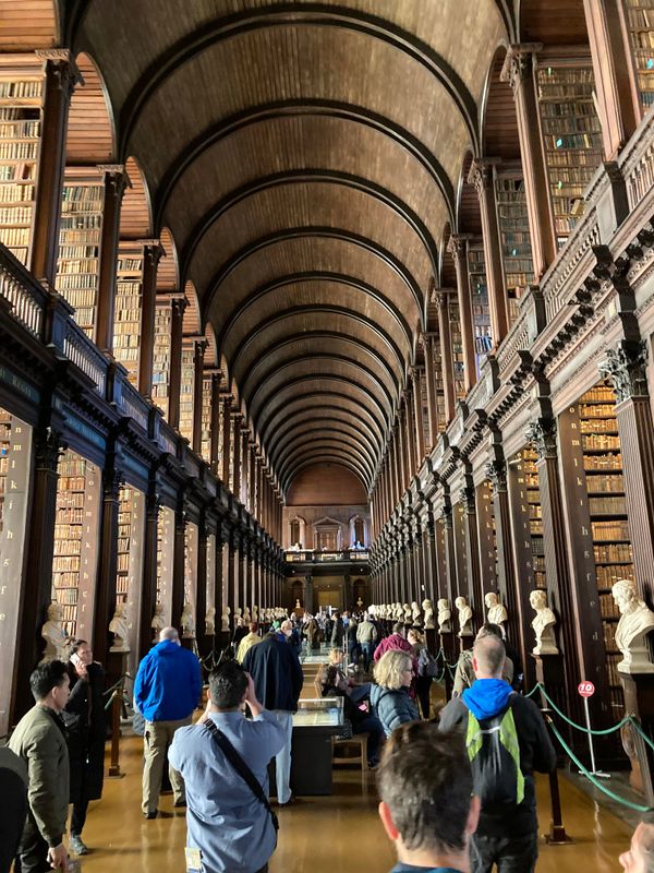 A photof the Old Library at Trinity College, two floors of bookshelves on the side and a bunch of people in the middle