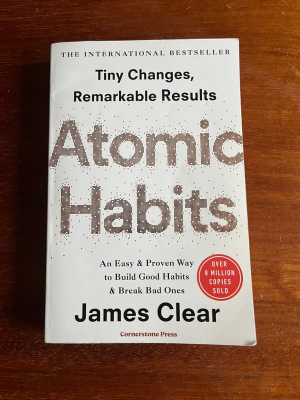 The book Atomic Habits lying on a brown wooden tab